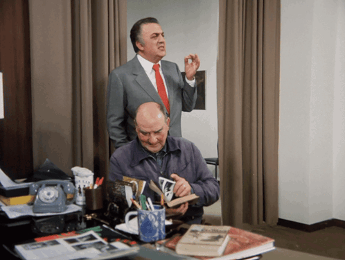 Man in Suit Behind Man at Desk With Book
