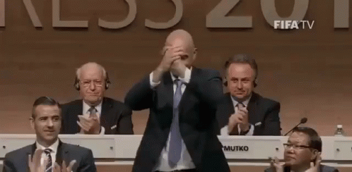 Man in Suit Covering Face While Men Applaud