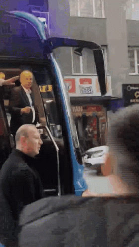 Man In Suit Exits Blue Bus At Fan Sign GIF