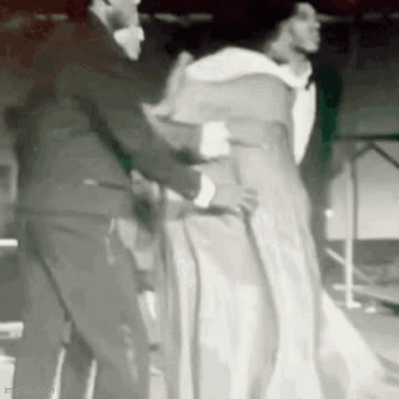 Man in Suit Helping Woman in White Dress with Cane