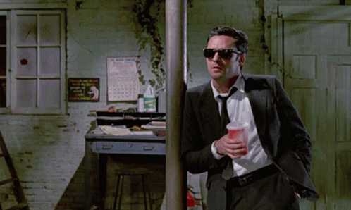 Man in Suit Holding Cup Leaning on Pole