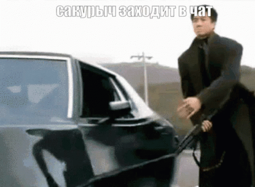 Man in Suit Holding Gun in Front of Car with Foreign Caption