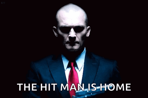 Man in Suit Holding Gun Saying The Hit Man is Home