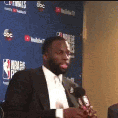 Man in Suit Holding Microphone at Blue Wall Saying NBA