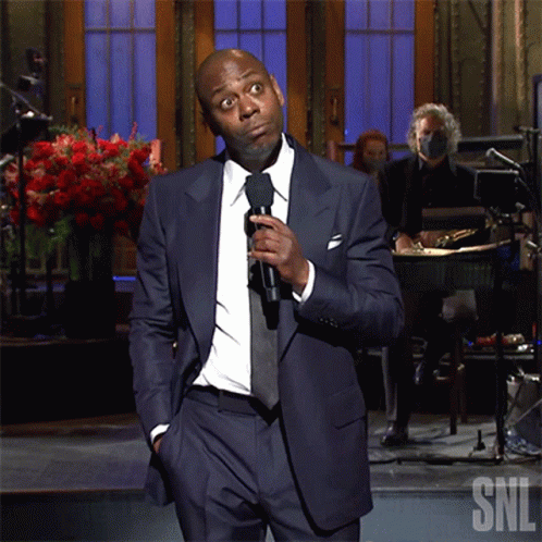 Man In Suit Holding Microphone In Front Of SNL Logo GIF