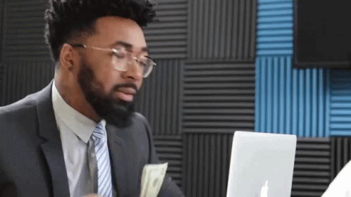 Man in Suit Holding Money in Front of Laptop