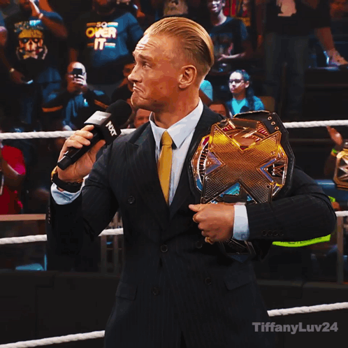 Man in Suit Holding Wrestling Championship Belt Talking Into Microphone