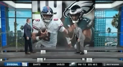 Man in Suit in Front of Screen With Two Football Players