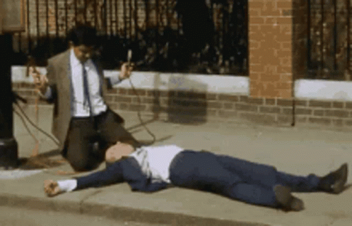 Man in Suit Kneeling Beside Man on Sidewalk