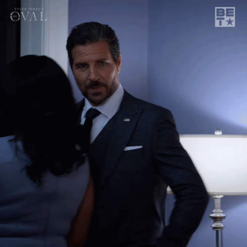 Man In Suit Next To Woman By Blue Wall Saying Oval GIF