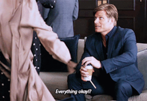 Man in Suit on Couch Talking to Man Holding Coffee