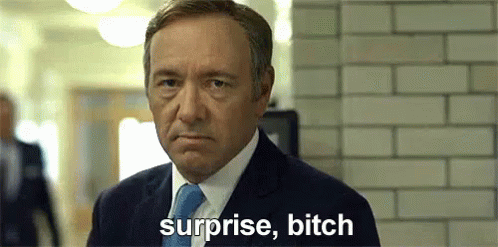 Man in Suit Saying Surprise Bitch in Front of Brick Wall