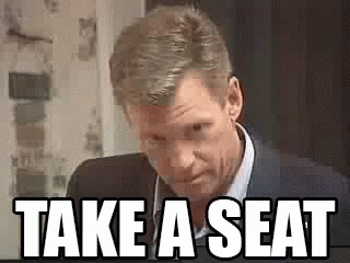 Man In Suit Saying Take A Seat GIF