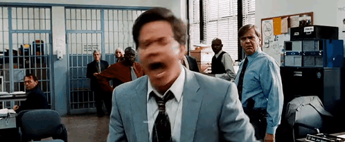 Man In Suit Screaming In Police Station With Group Behind Him GIF