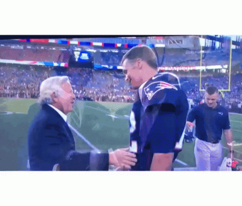 Man in Suit Shaking Hands With Man in Patriots Jersey