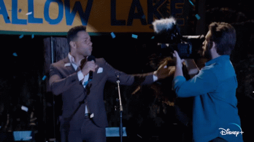 Man in Suit Singing Into Microphone While Cameraman Takes Picture