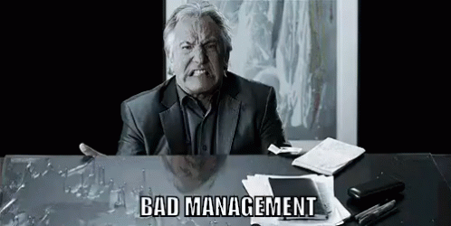 Man in Suit Sitting at Desk With Broken Glass Making Funny Face