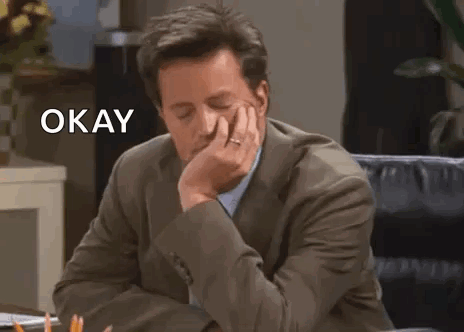Man in Suit Sitting at Desk With Hand on Chin Saying Okay