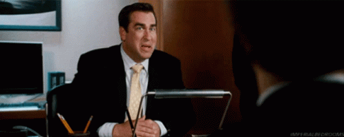 Man In Suit Sitting At Desk With Pow Behind Him GIF