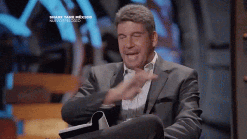 Man In Suit Sitting At Shark Tank Sign GIF