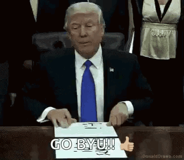Man in Suit Sitting at Table With Go BYU Sign
