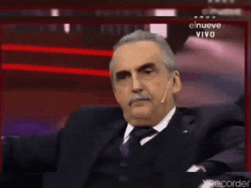 Man in Suit Sitting Before Screen Saying El Nueve Vivo