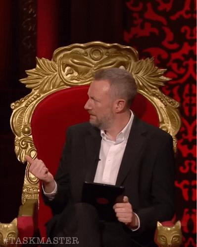 Man in Suit Sitting in Chair Taskmaster