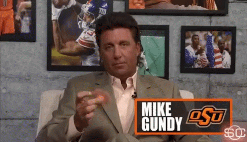 Man in Suit Sitting in Front of Mike Gundy Sign