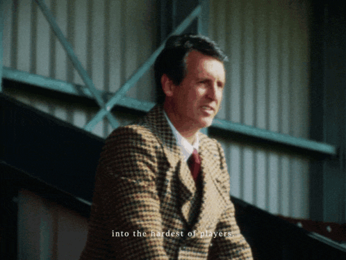 Man In Suit Sitting In Stadium In Front Of Play Sports Screen GIF