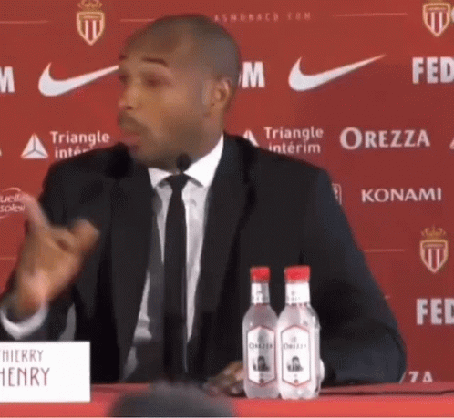 Man in Suit Speaking Into Microphone at Henry Sign