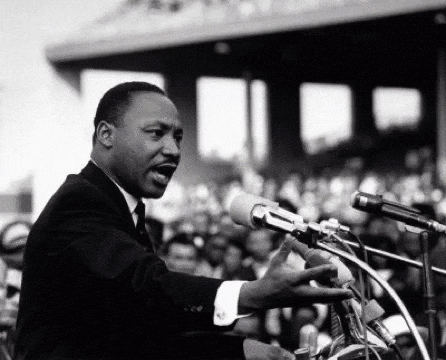Man in Suit Speaking Into Microphone Before Crowd