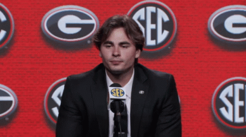 Man in Suit Speaking Into Microphone Saying Seb