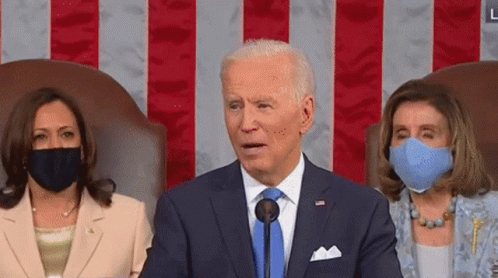 Man in Suit Speaking Into Microphone With Two Masked Women