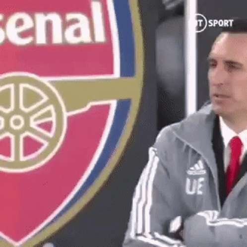 Man in Suit Standing Before Arsenal Logo