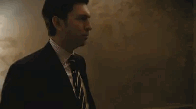 Man In Suit Standing By Blackboard In Dark Room GIF