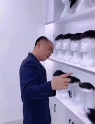 Man in Suit Standing by Mannequin Heads Shelf