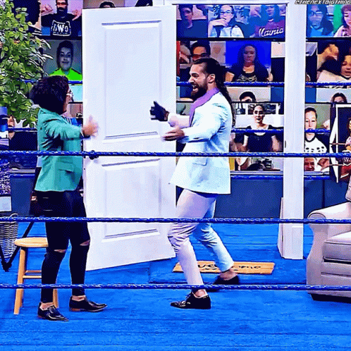 Man in Suit Standing in Wrestling Ring With Woman in Green Jacket