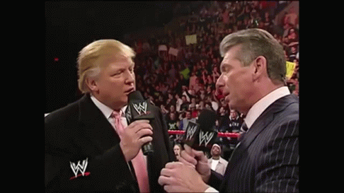 Man in Suit Talking Into Microphone Another Man Watching