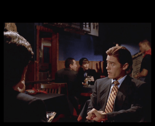 Man in Suit Talking to Another Man With Gotten Us In Behind Him