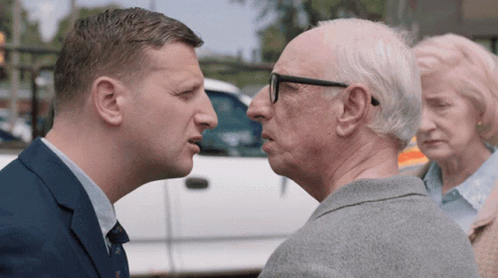 Man In Suit Talking To Older Man In Glasses GIF