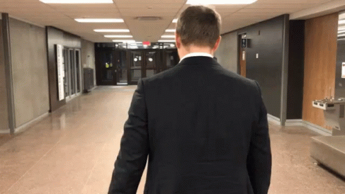 Man In Suit Walking Down Hallway With Water Fountain GIF