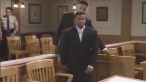 Man In Suit Walking In Courtroom With Man Behind GIF