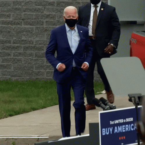 Man In Suit Walking Past Sign Saying Buy America GIF