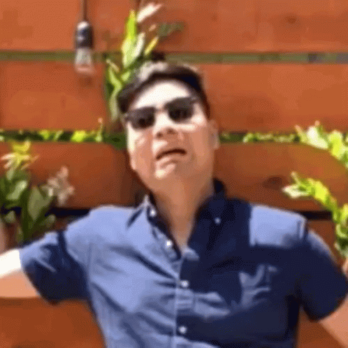 Man in Sunglasses and Hat Making Funny Face in Front of Wooden Wall