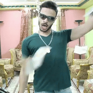 Man in Sunglasses and Necklace With Arms Outstretched in Living Room