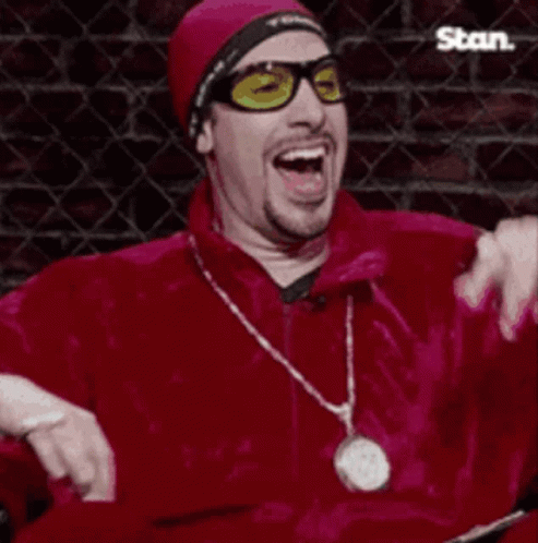 Man in Sunglasses and Red Jacket Laughing With Der war böse Sign