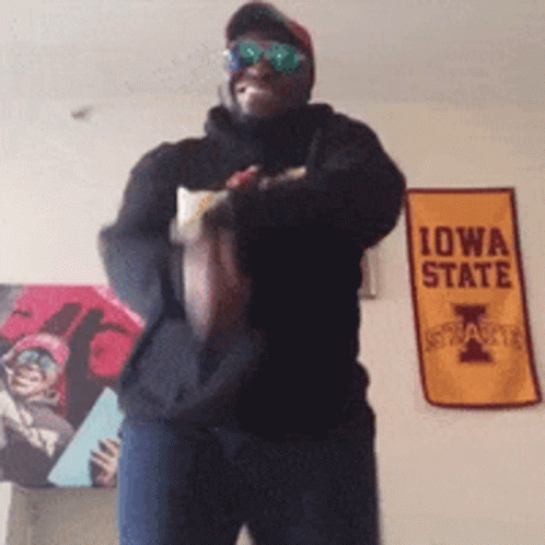 Man in Sunglasses Holding Football in Front of Iowa State Sign
