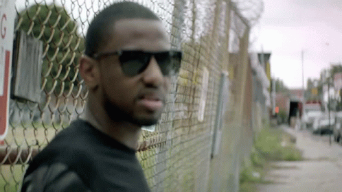 Man in Sunglasses Leaning Against Chain Link Fence