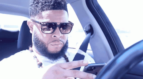 Man in Sunglasses Looking at Phone While Driving