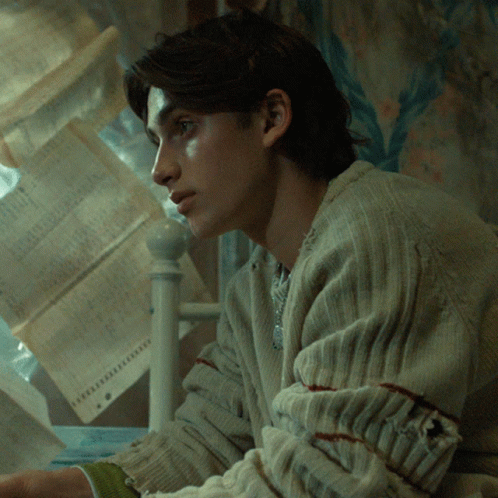 Man In Sweater In Front Of Paper Stack GIF